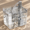 High view into the wide drinking tray of a transparent cat water fountain, water from the spout rippling across the surface, on a sunlit wooden floor