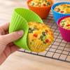 A hand peeling back a flexible green silicone case as a golden egg muffin comes out whole