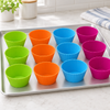 Twelve empty silicone muffin cases in green, orange, blue and pink standing on a flat baking tray, no tin