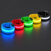 Five LED armbands lit on a dark surface: blue, red, green, yellow, and a black strap with a white light