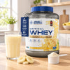Applied Nutrition Critical Whey 2kg Banana Milkshake tub with a scoop in a kitchen