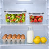 Two clear lidded produce containers side by side on a fridge shelf