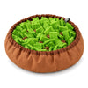 A round snuffle bowl on a white background, with a brown fabric rim and a bed of green felt strips hiding pieces of dry food.