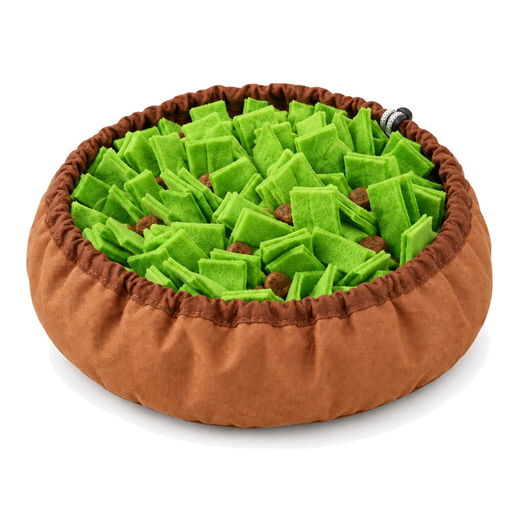 A round snuffle bowl on a white background, with a brown fabric rim and a bed of green felt strips hiding pieces of dry food.