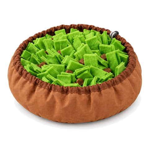 A round snuffle bowl on a white background, with a brown fabric rim and a bed of green felt strips hiding pieces of dry food.