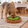 Christmas Day in a living room: a dog forages in a green felt snuffle bowl on the rug while the Christmas table is laid in the background