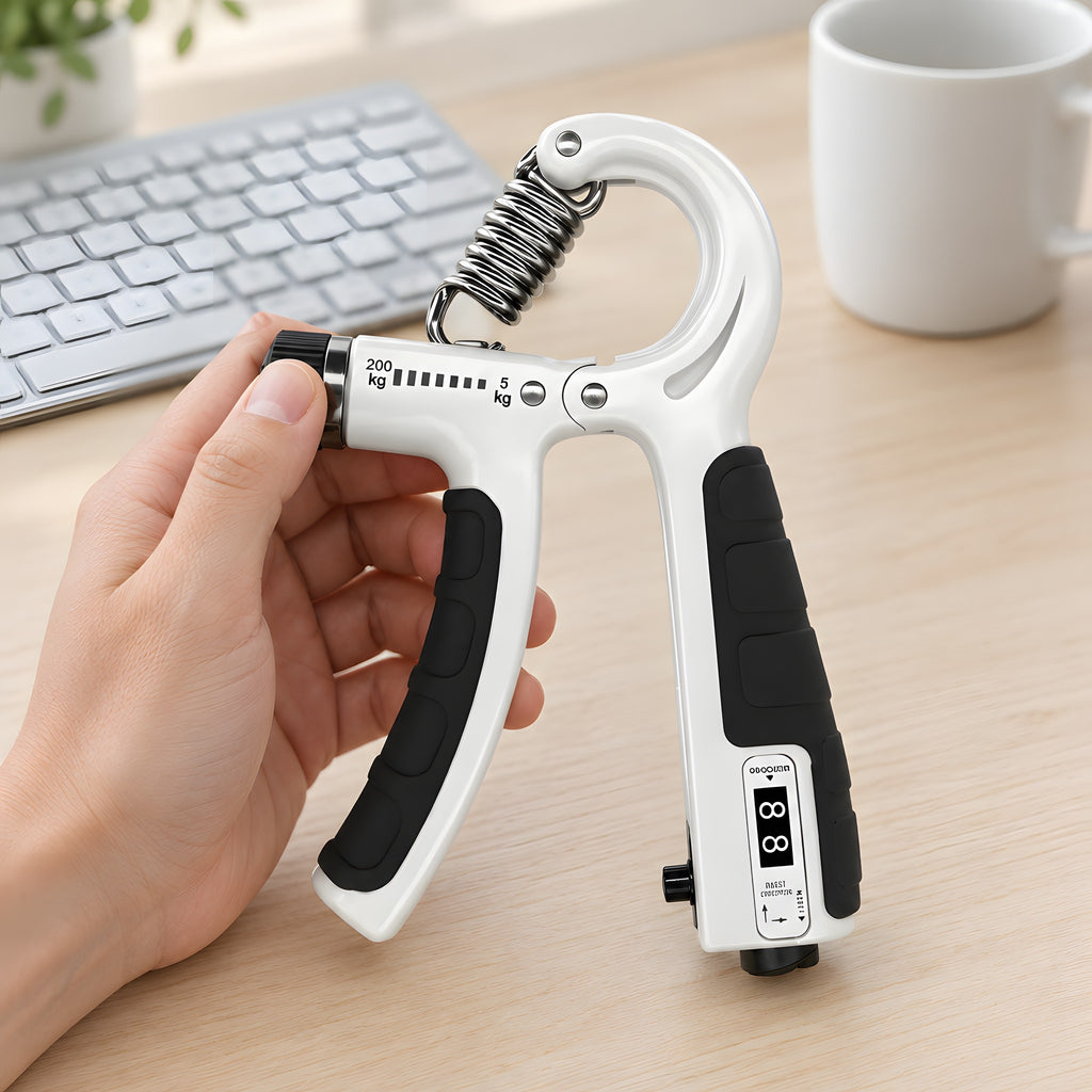A thumb turning the dial of the white grip trainer at a light desk, beside a keyboard and a mug