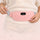 Hands adjusting the strap of the pink heated period belt worn around the waist over a cream sweater