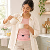 A smiling woman pouring tea in a bright kitchen with the pink heated period belt worn at her waist