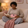 A woman reading on a sofa in the evening under a pink blanket with the pink heated period belt at her waist